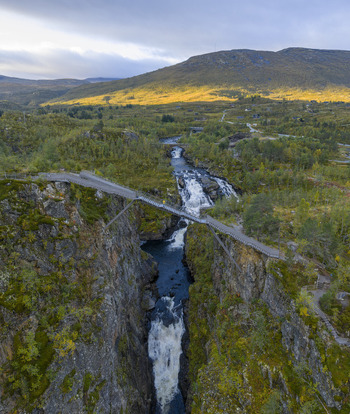Aerial view of Voringfossen waterfall and the modern pedestrian bridge spanning the deep canyon with lush green hills Eidfjord Municipality Vestland Norway.