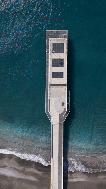 Aerial view of a pier stretching into the turquoise sea contrasting with the dark sandy beach Minori Salerno Italy Aerial view of a pier stretching into the turquoise sea contrasting with the dark sandy beach Minori Salerno Italy