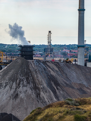 Aerial view of the Tata Steel industrial plant with a large pile of raw material smoking chimney and industrial cranes in Velsen Noord Noord Holland Netherlands. Aerial view of the Tata Steel industrial plant with a large pile of raw material smoking chimney and industrial cranes in Velsen Noord Noord Holland Netherlands.