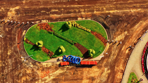 Aerial view of a roundabout under construction with green landscaping small trees and piles of blue and orange construction pipes on the dirt ground Latvia. Aerial view of a roundabout under construction with green landscaping small trees and piles of blue and orange construction pipes on the dirt ground Latvia.