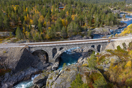 Aerial view of a stone railway bridge crossing a river surrounded by autumn foliage and rocky terrain in Bjorli Innlandet Norway. Aerial view of a stone railway bridge crossing a river surrounded by autumn foliage and rocky terrain in Bjorli Innlandet Norway.