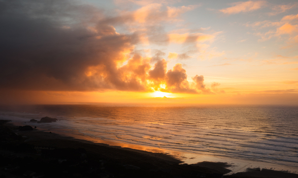 Aerial view of a dramatic sunset over the Pacific Ocean beach with dark storm clouds gathering over the horizon and golden light reflecting on the wet sand Bandon Oregon United States. Aerial view of a dramatic sunset over the Pacific Ocean beach with dark storm clouds gathering over the horizon and golden light reflecting on the wet sand Bandon Oregon United States.