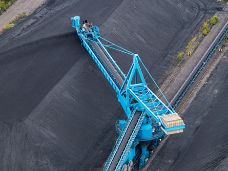 Aerial view of a large blue industrial stacker machine operating at a coal mining site with massive black coal piles and conveyor belt systems in Berlin Berlin Germany.
