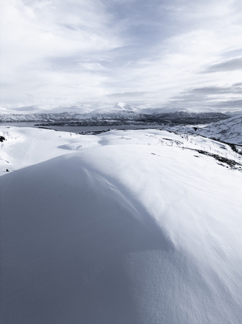 Aerial view of snow covered rolling hills and a distant fjord under an overcast winter sky in Kvaloya Troms Norway. Aerial view of snow covered rolling hills and a distant fjord under an overcast winter sky in Kvaloya Troms Norway.