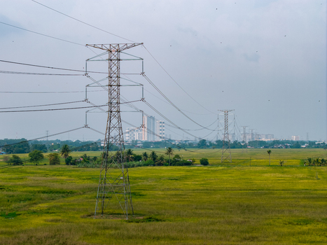 Aerial view of a transmission tower standing in a vast green field with distant buildings under a hazy sky in Bukit Mertajam Penang Malaysia. Aerial view of a transmission tower standing in a vast green field with distant buildings under a hazy sky in Bukit Mertajam Penang Malaysia.