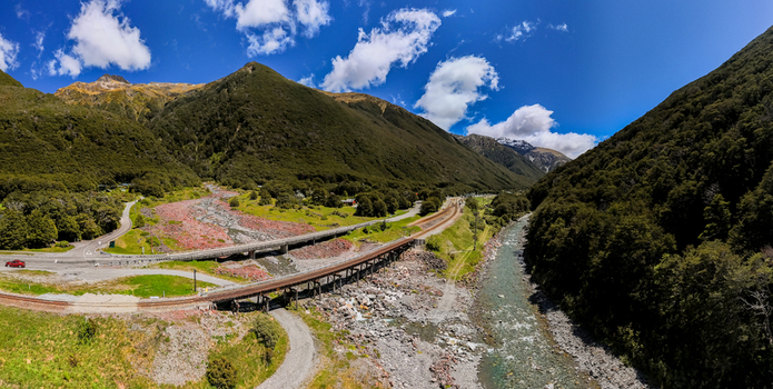 Aerial view of a railway bridge crossing a rocky riverbed in a lush mountainous valley in Canterbury Region New Zealand.