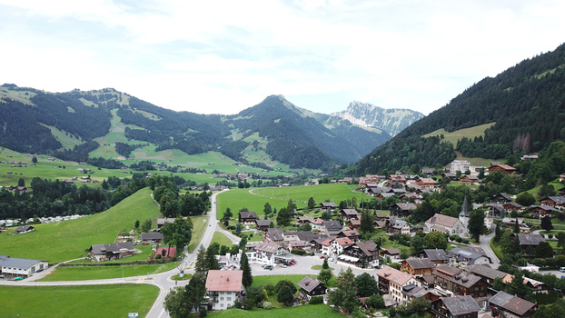 Aerial view of the alpine village of Chateau d Oex with traditional chalets and a church spire nestled among green hills and mountains in Chateau d Oex Vaud Switzerland. Aerial view of the alpine village of Chateau d Oex with traditional chalets and a church spire nestled among green hills and mountains in Chateau d Oex Vaud Switzerland.