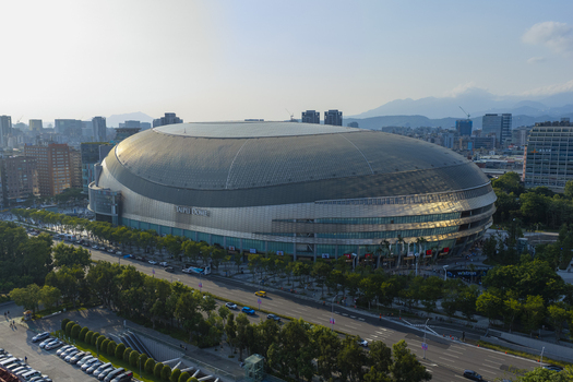 Aerial view of Taipei Dome stadium with its distinctive oval roof surrounded by urban streets lush trees and city buildings under a clear sky in Taipei Taiwan. Aerial view of Taipei Dome stadium with its distinctive oval roof surrounded by urban streets lush trees and city buildings under a clear sky in Taipei Taiwan.