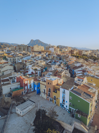 Aerial view of colorful houses and urban rooftops with a mountain peak in the background under a clear blue sky in La Vila Joiosa Valencian Community Spain. Aerial view of colorful houses and urban rooftops with a mountain peak in the background under a clear blue sky in La Vila Joiosa Valencian Community Spain.