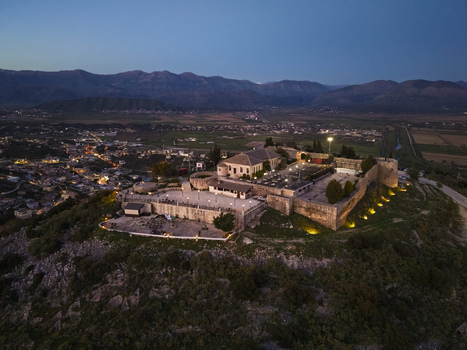 Aerial view of the illuminated Lekuresi Castle perched on a hill overlooking the town of Saranda at dusk with stone walls and a courtyard visible in Saranda Vlore County Albania. Aerial view of the illuminated Lekuresi Castle perched on a hill overlooking the town of Saranda at dusk with stone walls and a courtyard visible in Saranda Vlore County Albania.