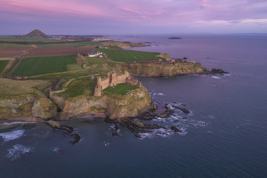 Aerial view of Tantallon Castle on a rugged cliff overlooking the sea under a pink sunset sky North Berwick Scotland United Kingdom.