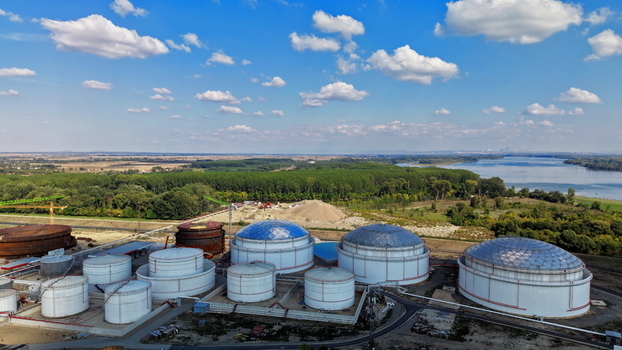 Aerial view of industrial fuel tanks situated near a river surrounded by lush green trees and open fields under a bright blue sky in Kovin Vojvodina Serbia. Aerial view of industrial fuel tanks situated near a river surrounded by lush green trees and open fields under a bright blue sky in Kovin Vojvodina Serbia.
