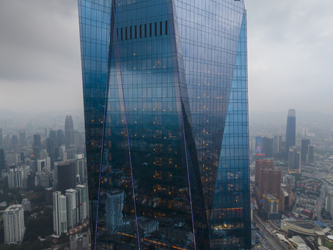 Kuala Lumpur Malaysia 09 March 2026 Aerial view of the modern glass facade of a skyscraper with the city skyline and hazy mountains in the background.