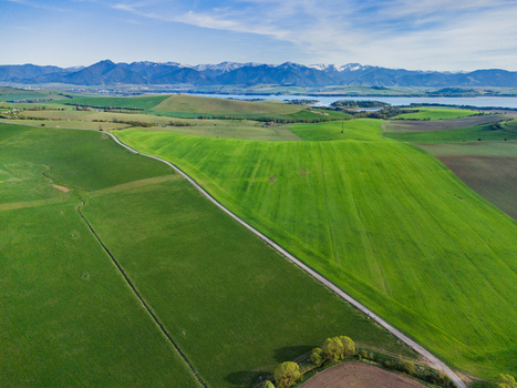 Aerial view of lush green fields and rolling hills overlooking the Liptovska Mara reservoir with the Tatra Mountains in the distance under a clear blue sky Liptovske Matiasovce Zilina Region Slovakia.