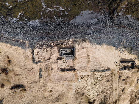 Aerial view of the ruins of an abandoned farmhouse on sandy terrain near a dark rocky shoreline in Hafnarfjordur Hafnarfjardarkaupstad Iceland.