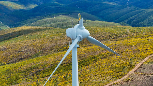 Aerial view of a wind turbine standing on a hilly landscape covered with yellow flowering bushes and green vegetation in Lisbon Lisbon Portugal. Aerial view of a wind turbine standing on a hilly landscape covered with yellow flowering bushes and green vegetation in Lisbon Lisbon Portugal.