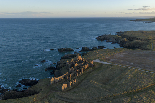 Aerial view of the ruins of Slains Castle on a grassy cliff overlooking the North Sea during golden hour in Cruden Bay Scotland United Kingdom. Aerial view of the ruins of Slains Castle on a grassy cliff overlooking the North Sea during golden hour in Cruden Bay Scotland United Kingdom.
