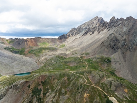 Aerial view of Mount Sneffels and the rugged landscape of Yankee Boy Basin in the San Juan Mountains with a winding trail and alpine lake in Ouray County Colorado United States. Aerial view of Mount Sneffels and the rugged landscape of Yankee Boy Basin in the San Juan Mountains with a winding trail and alpine lake in Ouray County Colorado United States.