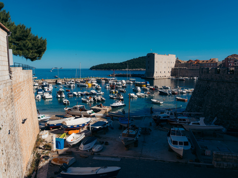 View of the historic old port with small boats moored in the turquoise water by the stone walls of Dubrovnik Old Town Dubrovnik Dubrovnik Neretva County Croatia. View of the historic old port with small boats moored in the turquoise water by the stone walls of Dubrovnik Old Town Dubrovnik Dubrovnik Neretva County Croatia.
