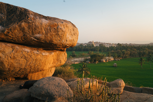 View of large granite boulders overlooking lush green fields and ancient temple ruins in the landscape of Hampi Karnataka India. View of large granite boulders overlooking lush green fields and ancient temple ruins in the landscape of Hampi Karnataka India.
