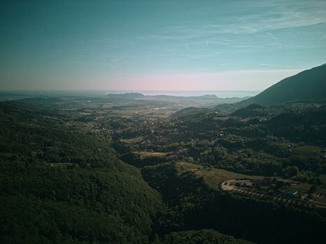 Aerial view of Lake Garda in the distance with lush green forested hills and a valley under a clear blue sky in Italy.