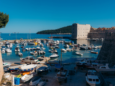 View of the historic Old Port with numerous small boats moored in front of St. John s Fortress under a clear blue sky in Dubrovnik Dubrovnik Neretva County Croatia. View of the historic Old Port with numerous small boats moored in front of St. John s Fortress under a clear blue sky in Dubrovnik Dubrovnik Neretva County Croatia.