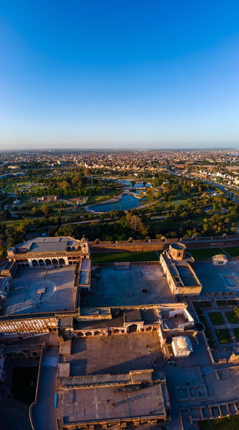 Aerial view of Lahore Fort featuring historic courtyards and surrounding parkland with the city skyline in the distance under a clear blue sky in Lahore Punjab Pakistan.