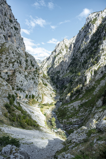 View of a dramatic gorge carved through jagged sunlit cliffs revealing patches of green vegetation and a winding trail below Picos de Europa Asturias Spain. View of a dramatic gorge carved through jagged sunlit cliffs revealing patches of green vegetation and a winding trail below Picos de Europa Asturias Spain.