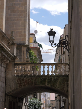 View of a stone archway with a balustrade connecting historic buildings in the old town featuring an ornate street lamp and a construction crane in Ourense Province of Ourense Spain.