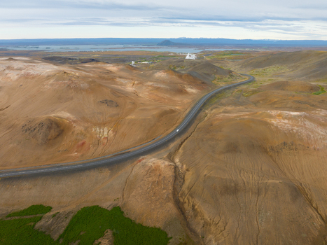 Aerial view of a ribbon of asphalt winding through a desolate landscape of ochre and brown hues contrasting with the distant pale blue horizon Reykjahl&iacute;&eth; &THORN;ingeyjarsveit Iceland.