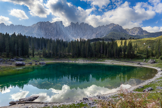 View of Karersee with the Latemar mountain range reflected in the turquoise water surrounded by a dense pine forest in Welschnofen Trentino Alto Adige Italy.