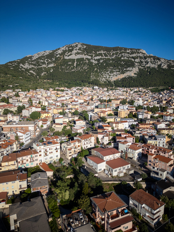 Aerial view of the town of Dorgali nestled at the foot of a rugged limestone mountain with terracotta rooftops and dense urban architecture under a clear blue sky Dorgali Sardinia Italy. Aerial view of the town of Dorgali nestled at the foot of a rugged limestone mountain with terracotta rooftops and dense urban architecture under a clear blue sky Dorgali Sardinia Italy.