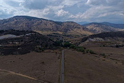 Aerial view of a winding road cutting through the dry rolling foothills of the Rocky Mountains under a cloudy sky in Golden Colorado United States.