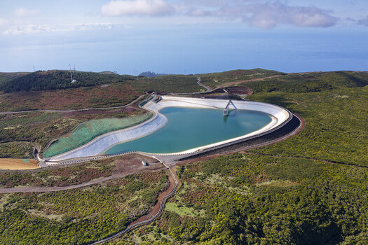 Aerial view of the Bica da Cana reservoir with its turquoise water and concrete embankment surrounded by lush green hills and distant ocean in Funchal Madeira Portugal.