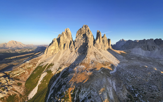 Aerial view of rugged peaks of Tre Cime di Lavaredo pierce the sky casting long shadows across the alpine landscape Tre Cime di Lavaredo Belluno Italy. Aerial view of rugged peaks of Tre Cime di Lavaredo pierce the sky casting long shadows across the alpine landscape Tre Cime di Lavaredo Belluno Italy.