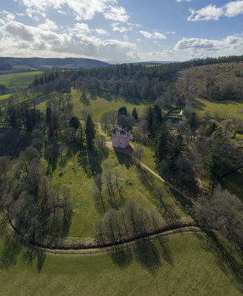Aerial view of Craigievar Castle surrounded by lush green fields and dense woodland under a bright sky Craigievar Scotland United Kingdom.