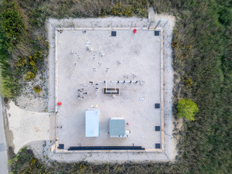Aerial view of a fenced industrial utility site with pipes and small buildings on a gravel surface surrounded by vegetation in Teulada Valencian Community Spain.