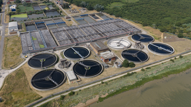 Aerial view of the Long Reach Sewage Treatment Works featuring circular sedimentation tanks and rectangular treatment basins situated near the riverbank in Dartford England United Kingdom.
