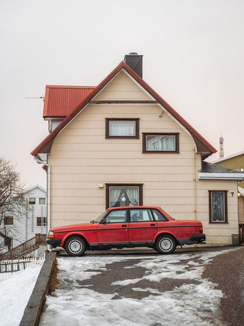 View of a striking red car parked before a quaint cream colored house with a red roof amidst the snowy landscape Henningsv&aelig;r Nordland Norway.