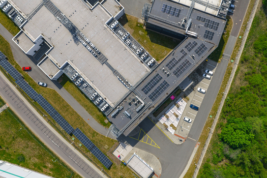 Aerial view of a modern industrial building with rooftop solar panels and HVAC units adjacent parking lot with cars and surrounding greenery in Prague Prague Czechia.