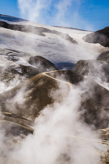 View of a winding road cut through a misty otherworldly landscape beneath a glacier under a bright blue sky Hrunamannahreppur Hrunamannahreppur Iceland.
