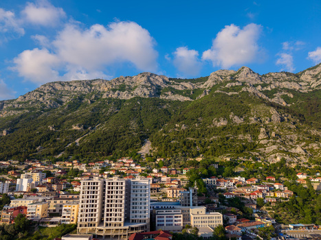 Aerial view of the town of Kruje nestled at the foot of a massive rocky mountain with residential buildings green trees and white clouds in a blue sky Kruje Durres County Albania.
