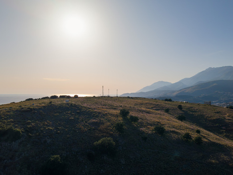 Aerial view of a grassy hill with communication towers overlooking the sea and distant mountains under a bright sun in Porto Palermo Qarku i Vlores Albania. Aerial view of a grassy hill with communication towers overlooking the sea and distant mountains under a bright sun in Porto Palermo Qarku i Vlores Albania.