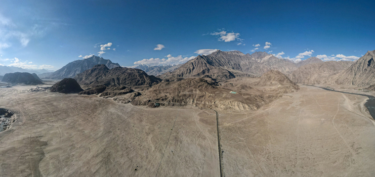 Aerial view of Sarfaranga Cold Desert Shigar with vast sandy dunes rugged mountain ranges and a winding river under a clear blue sky in Skardu Gilgit Pakistan.
