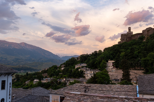 Gjirokaster Albania 09 June 2026 View of Gjirokaster Castle on a hill overlooking the historic stone rooftops and lush greenery under a sunset sky.
