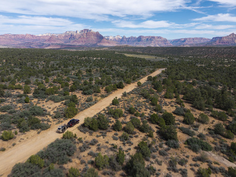 Aerial view of an SUV pulling a teardrop camper trailer along a dirt road on Gooseberry Mesa with red rock mountains of Zion National Park in Hurricane Utah United States. Aerial view of an SUV pulling a teardrop camper trailer along a dirt road on Gooseberry Mesa with red rock mountains of Zion National Park in Hurricane Utah United States.