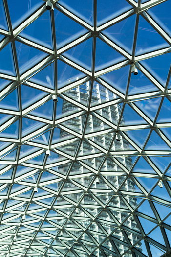 View of a modern geometric glass roof structure with a skyscraper visible through the transparent panels under a clear blue sky Bratislava Bratislava Region Slovakia. View of a modern geometric glass roof structure with a skyscraper visible through the transparent panels under a clear blue sky Bratislava Bratislava Region Slovakia.