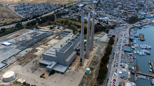 Aerial view of the Morro Bay Power Plant featuring three tall smokestacks beside the harbor and coastal town in Morro Bay California United States.
