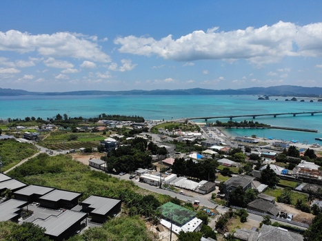 Aerial view of Kouri Bridge stretching across turquoise waters towards Kouri Island surrounded by lush coastal greenery and a clear blue sky in Nakijin Okinawa Japan. Aerial view of Kouri Bridge stretching across turquoise waters towards Kouri Island surrounded by lush coastal greenery and a clear blue sky in Nakijin Okinawa Japan.