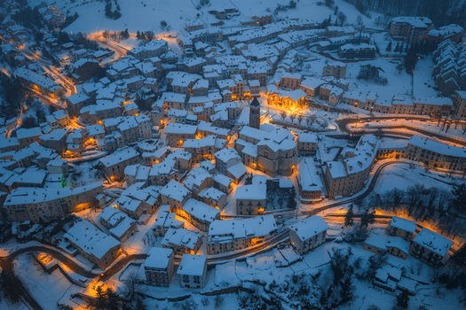Aerial view of the village of Rivisondoli covered in snow with illuminated buildings and winding roads at dusk in Rivisondoli Abruzzo Italy.